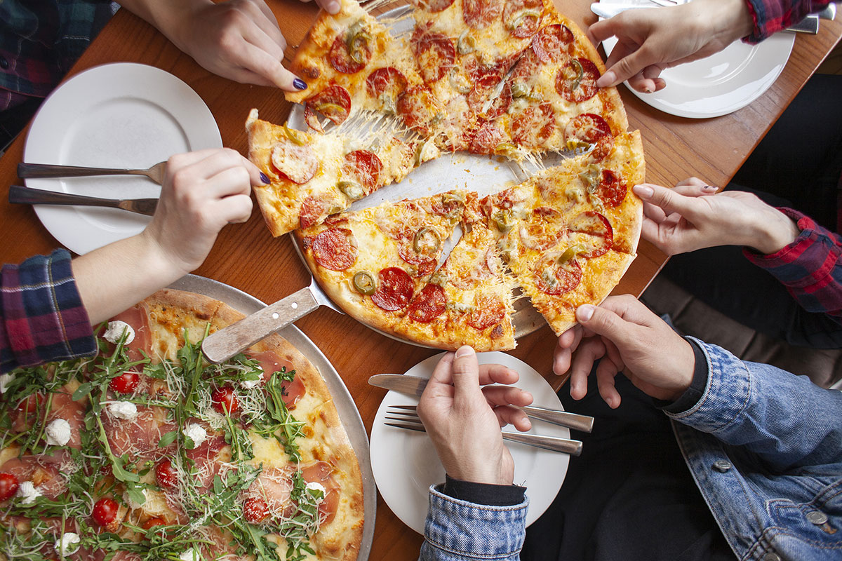 group of friends grabbing slices of pizza at restaurant